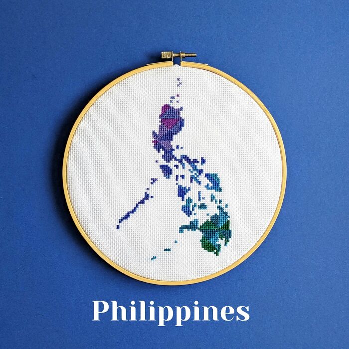 Cross-stitched map of the Philippines in an embroidery hoop on a blue background, showcasing detailed stitching and colors.