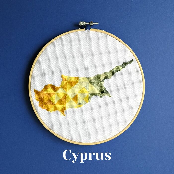Cross-stitched map of Cyprus with geometric patterns in yellow and green shades in an embroidery hoop on blue background