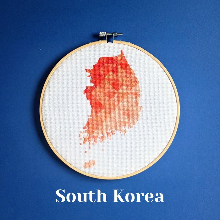 Cross-stitched map of South Korea in shades of red and orange displayed in an embroidery hoop on a blue background