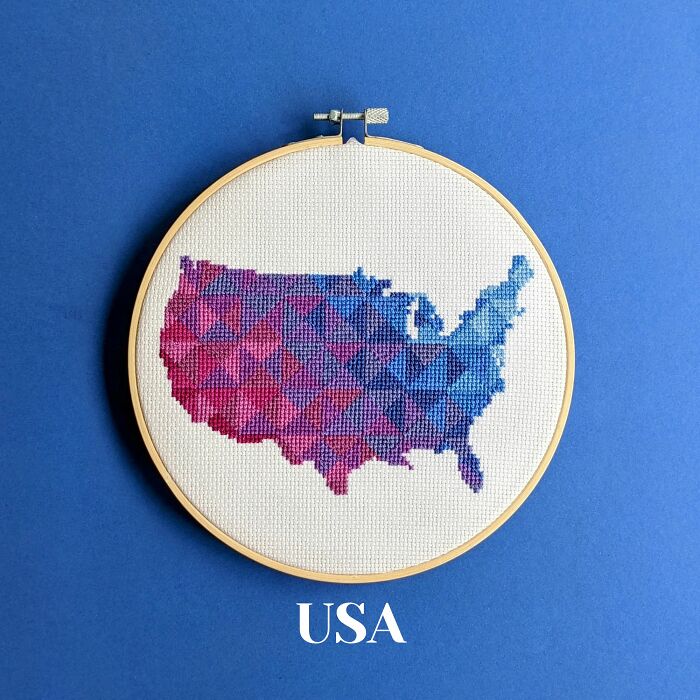 Cross-stitched map of the USA with a geometric pattern in shades of blue and purple in an embroidery hoop on a blue background.