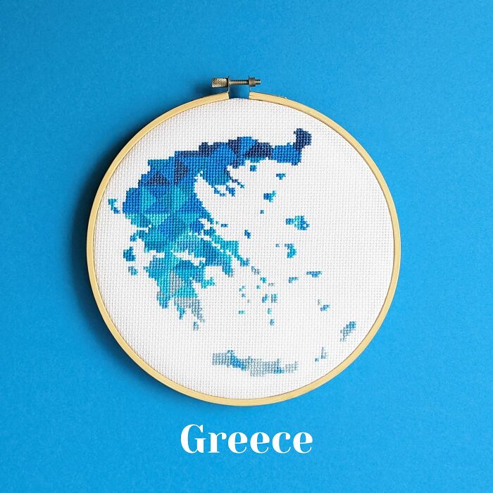 Cross-stitched map of Greece in shades of blue in an embroidery hoop on a bright blue background.