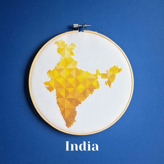 Cross-stitched map of India in shades of yellow and orange displayed in an embroidery hoop on blue background.