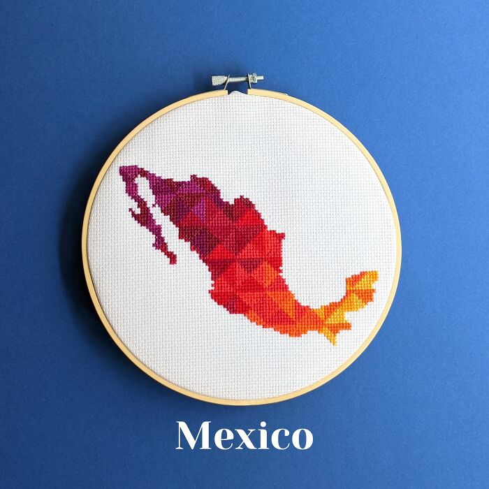 Cross-stitched map of Mexico in red and orange tones displayed on fabric within an embroidery hoop on blue background.