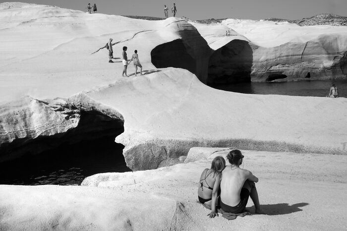 Black and white cinematic photo of people exploring unique rock formations and coastal caves in a natural landscape.