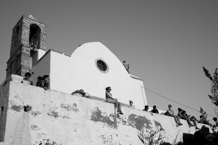 People sitting on the edge of a whitewashed building under clear sky in cinematic photos capturing everyday life moments.