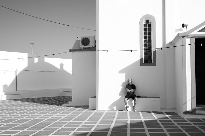 Man sitting alone on a bench casting a shadow in a minimalist courtyard featured in cinematic photos by Adriana Ferrarese.
