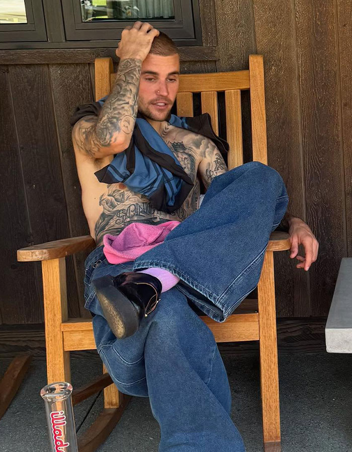 Young man with tattoos sitting shirtless on wooden chair, showing real dad and real husband confidence in casual setting. Young man with tattoos sitting shirtless on wooden chair, showing real dad and real husband confidence in casual setting.