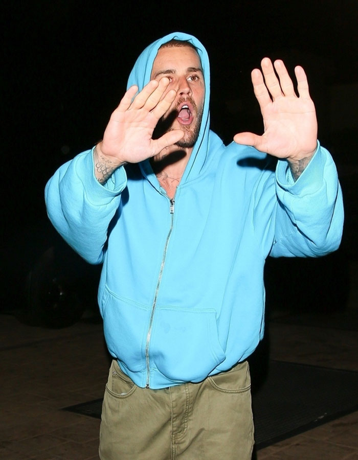 Justin Bieber wearing a blue hoodie, raising hands in a wild exchange with paparazzi at night outdoors. Justin Bieber wearing a blue hoodie, raising hands in a wild exchange with paparazzi at night outdoors.