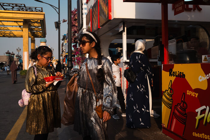 Two girls in shiny dresses standing on a street, captured by a photographer traveling the world capturing candid street moments.
