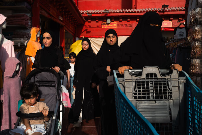 Women in traditional black attire and children walking through a vibrant street, capturing candid street moments full of emotion.