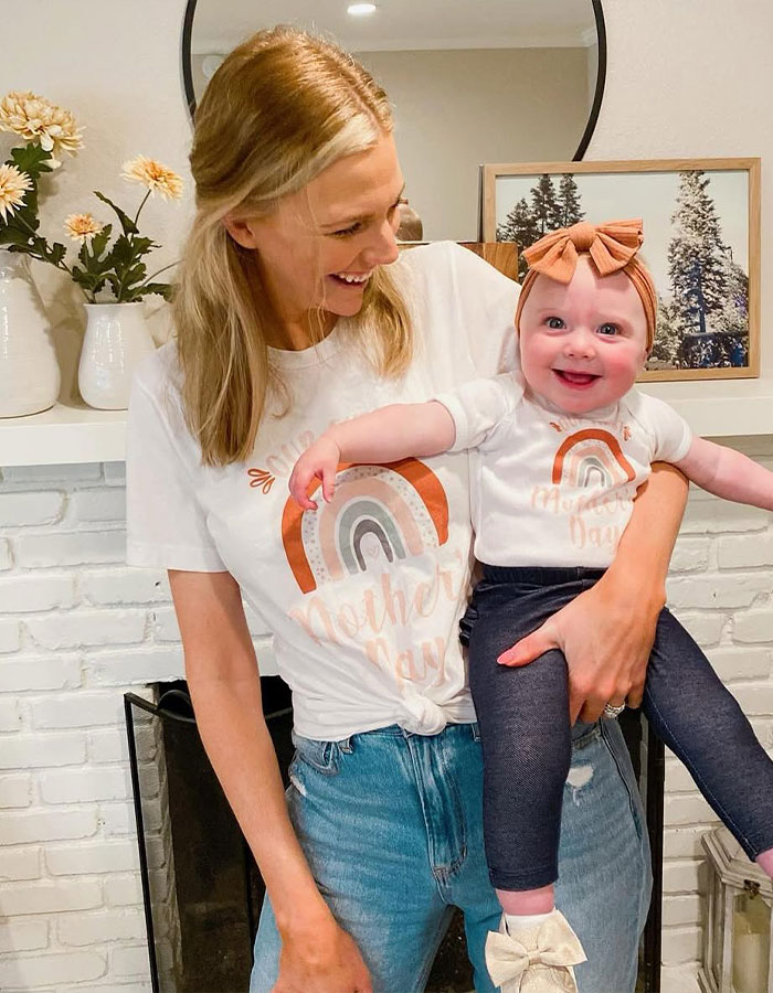 Mother joyfully holding smiling baby girl wearing matching Mother's Day shirts, representing real housewives exec and children. Mother joyfully holding smiling baby girl wearing matching Mother's Day shirts, representing real housewives exec and children.