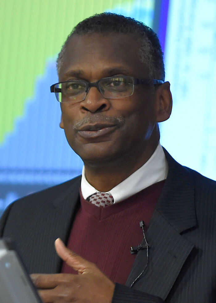 African American man in a suit and glasses speaking about world-changing inventions by people of color in a professional setting.