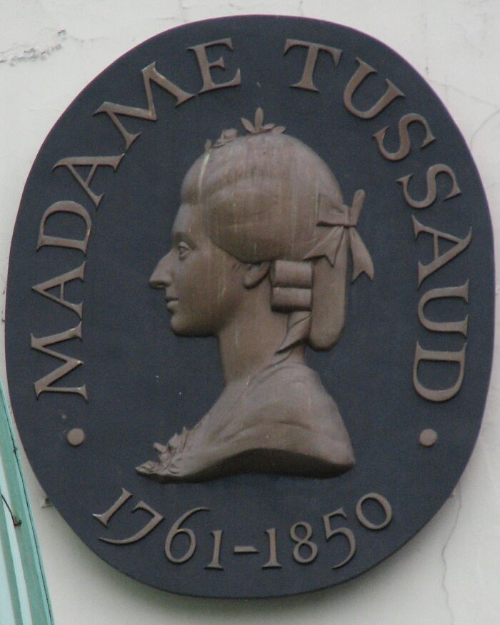 Plaque featuring a relief of Madame Tussaud, related to historical facts about Da Vinci and wedding planning.