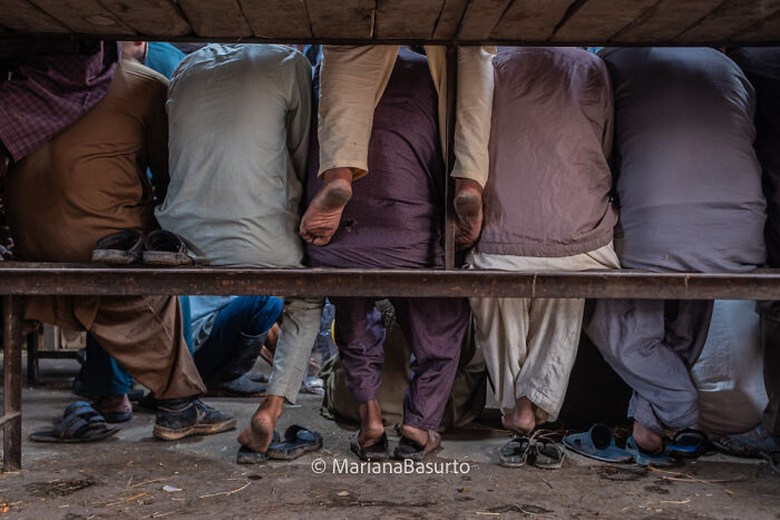 Group of people seated on a bench showing worn shoes and feet, capturing unseen realities through photography.