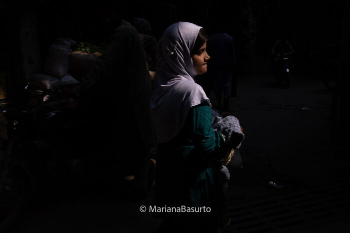 Young girl wearing a headscarf illuminated in dark street, capturing unseen realities of our world through photography.