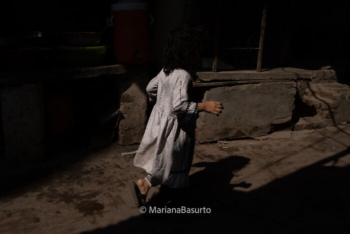 Child in worn dress walking in dim light, capturing unseen realities through powerful photography.