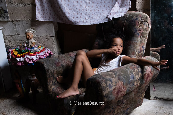 Child relaxing in a worn floral armchair, captured by a photographer revealing the unseen realities of our world.