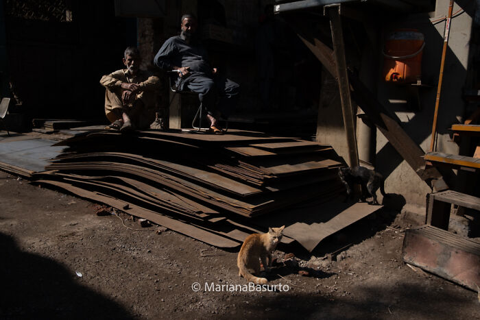 Two men sitting on stacked metal sheets in low light, showcasing unseen realities captured by a photographer.