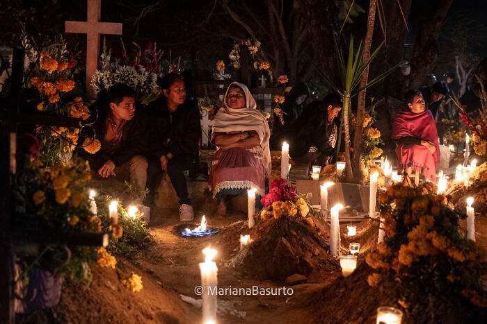 Photographer reveals unseen realities with a night scene of people honoring ancestors surrounded by candles and flowers.