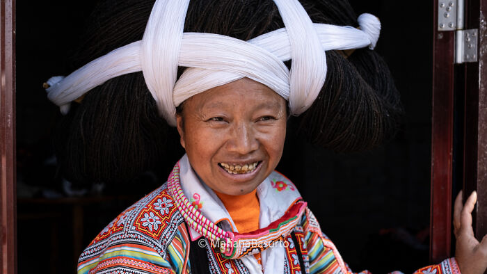 Smiling woman in traditional colorful clothing and elaborate headdress, capturing the unseen realities of our world through photography.