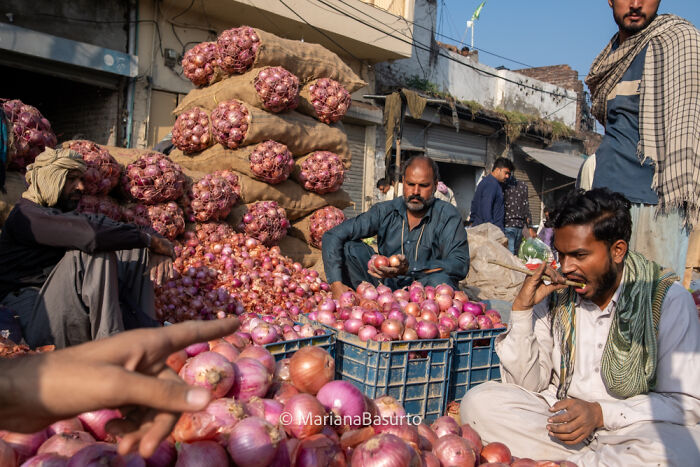 Photographer reveals unseen realities of daily life as men sort and sell onions in a busy outdoor market setting.
