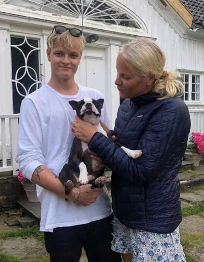 Young man holding a dog outside a house with a woman, related to Norwegian Crown Princess’s son charges news. Young man holding a dog outside a house with a woman, related to Norwegian Crown Princess’s son charges news.