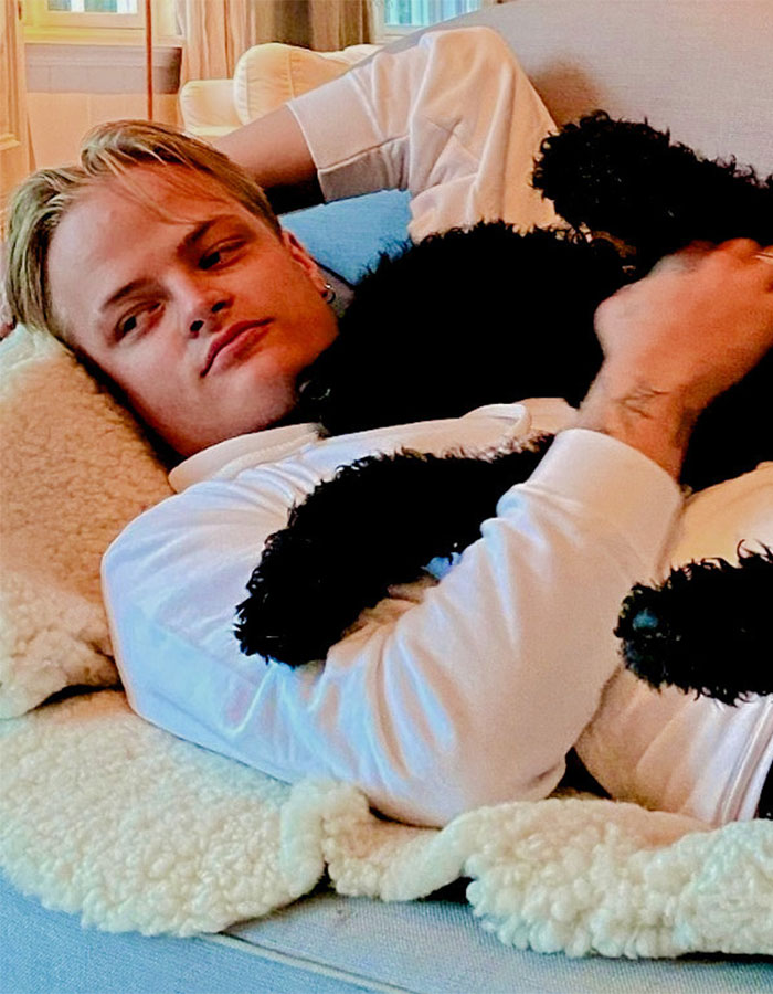 Norwegian Crown Princess’s son lying on a couch, holding a black dog, in a relaxed indoor setting.