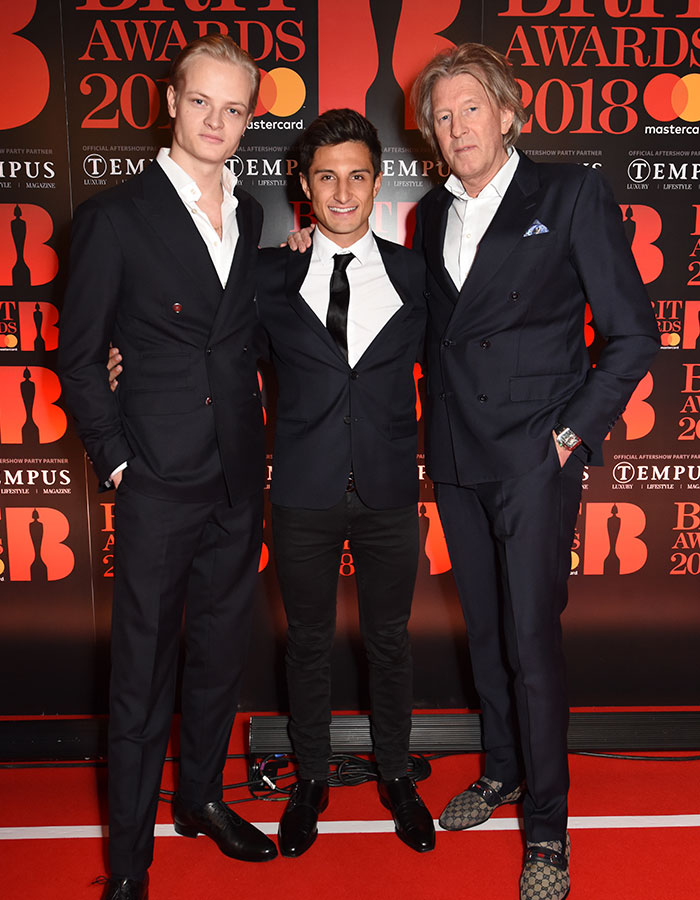 Three men dressed in suits posing on the red carpet at the BRIT Awards 2018 event.