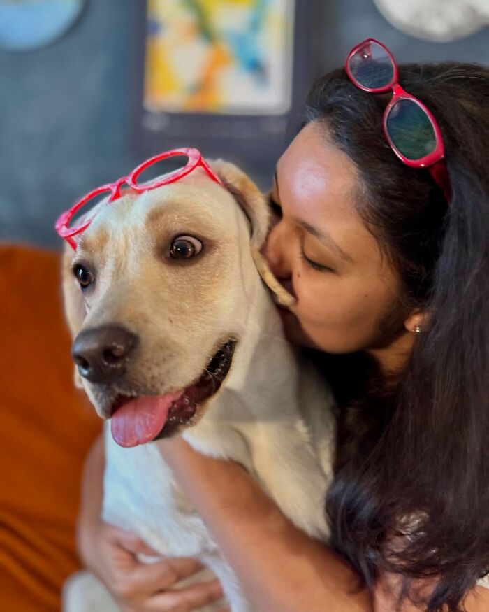 Woman hugging a rescue Labrador wearing red glasses, showcasing the Labrador's unique talent for painting with her mouth. Woman hugging a rescue Labrador wearing red glasses, showcasing the Labrador's unique talent for painting with her mouth.