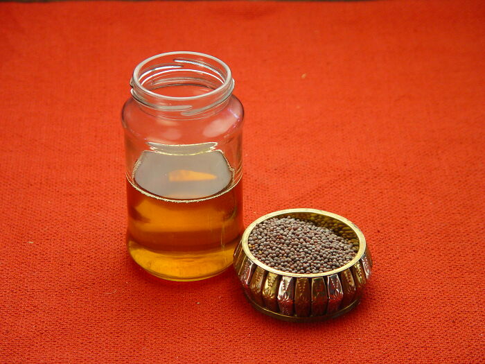 Jar of liquid and bowl of mustard seeds representing surprising foods banned in the USA on an orange background
