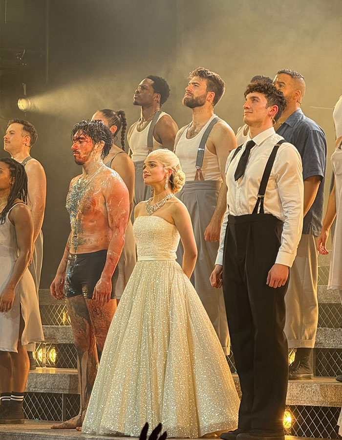 Rachel Zegler in a sparkling dress with cast members on stage during a live theatrical performance curtain call. Rachel Zegler in a sparkling dress with cast members on stage during a live theatrical performance curtain call.