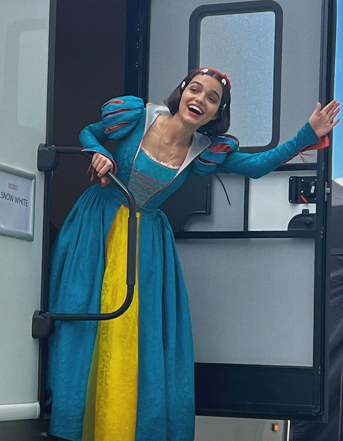 Rachel Zegler wearing Snow White costume, smiling and waving while standing in a trailer doorway during a live show. Rachel Zegler wearing Snow White costume, smiling and waving while standing in a trailer doorway during a live show.
