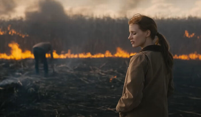 Woman in a brown jacket watches a fire burn in a field, a scene from one of the new millennium's greatest films.
