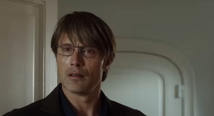 Man with glasses and brown hair looking concerned in a dimly lit room from new millennium greatest films.