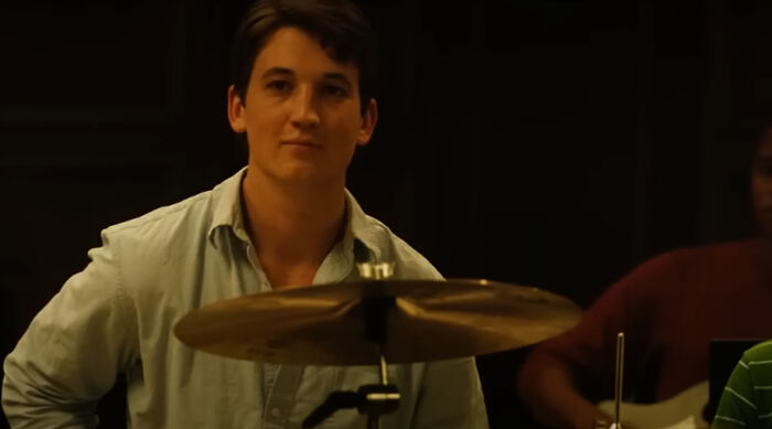 Young man playing drums in a dimly lit room, captured from a film scene featured in greatest films to see.