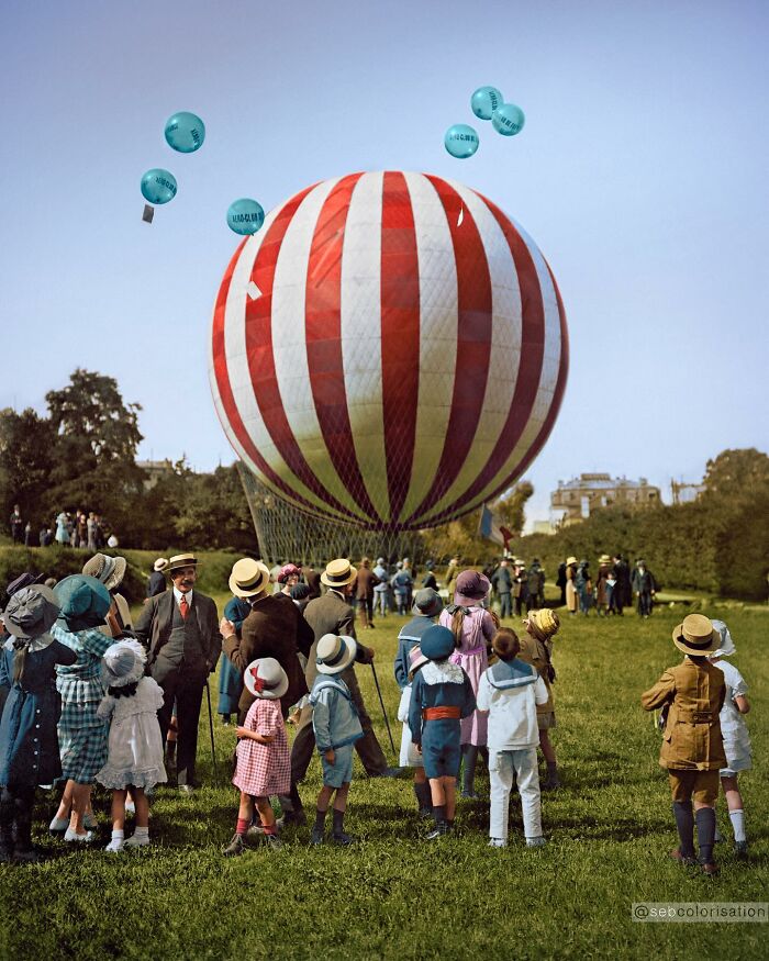 Children and adults gathered around a large striped hot air balloon in a magical historical photo colorized by viral artist.