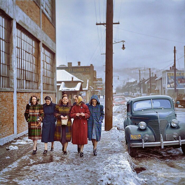 Five women in colorful vintage coats walking on a snowy street with a classic car, a magical historical photo colorized.