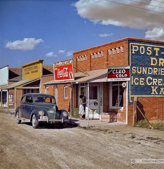 Colorized vintage photo of a rural grocery store and classic car on a dusty road from magical historical photos collection.