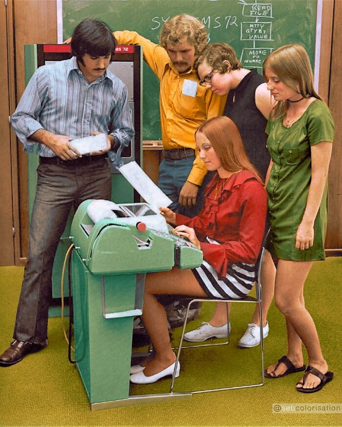 Group of young adults using an early computer terminal in a vintage setting, colorized by a talented viral artist.