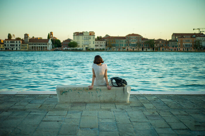 Woman sitting on a bench by the water, showcasing cinematic photos that highlight everyday life in a serene setting.