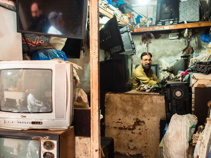 Man working in a cluttered space filled with old TVs, captured by photographer traveling the world capturing candid street moments.