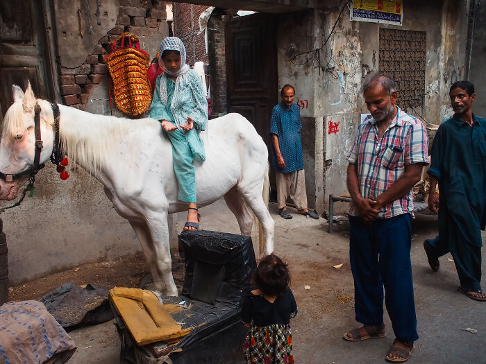 Child in traditional clothing sitting on a white horse in a narrow street captured by photographer traveling the world.