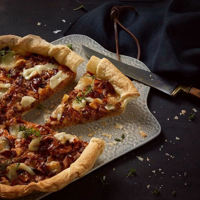 Close-up of a savory tart with melted cheese and herbs on a cutting board, featuring mouthwatering food photography.