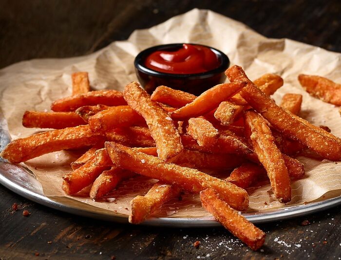 Crispy sweet potato fries served with ketchup on a plate, showcasing mouthwatering food photos by Kai Stiepel.