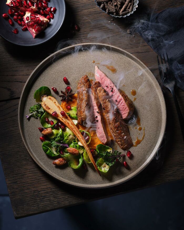 Steak slices with steamed vegetables and pomegranate seeds on a plate, showcasing mouthwatering food photography.