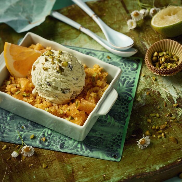 Mouthwatering food photo of creamy pistachio ice cream scoop on citrus fruit and grain mix in a white dish.
