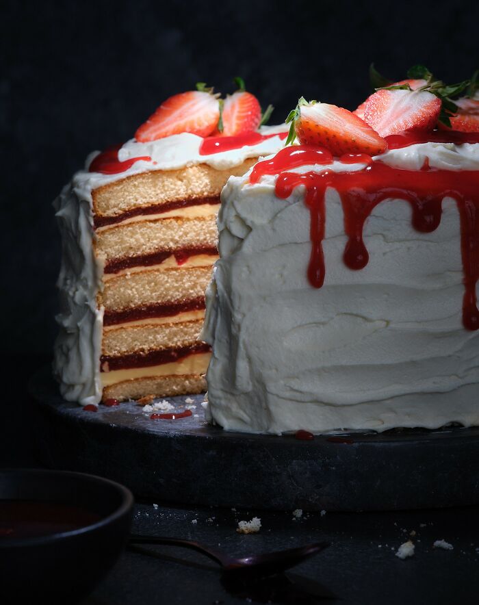 Layered cake with white frosting, strawberry topping, and red sauce drip, a mouthwatering food photo by Kai Stiepel.