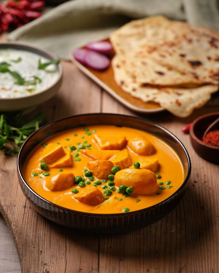 Creamy orange curry with peas and flatbread in the background, mouthwatering food photo by Kai Stiepel.