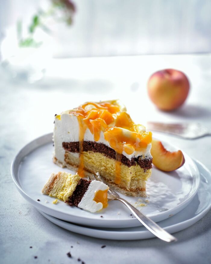 Slice of layered cake with fruit topping and sauce on a white plate, showcasing mouthwatering food photos by Kai Stiepel.