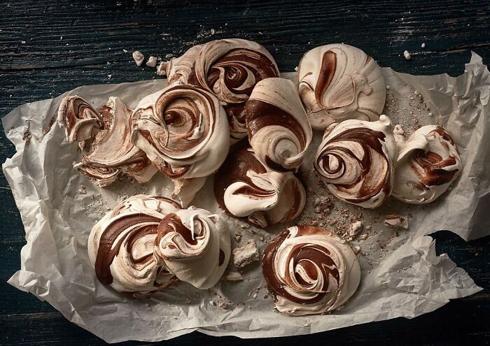 Swirled chocolate meringue cookies on parchment paper showcasing mouthwatering food photography by Kai Stiepel.